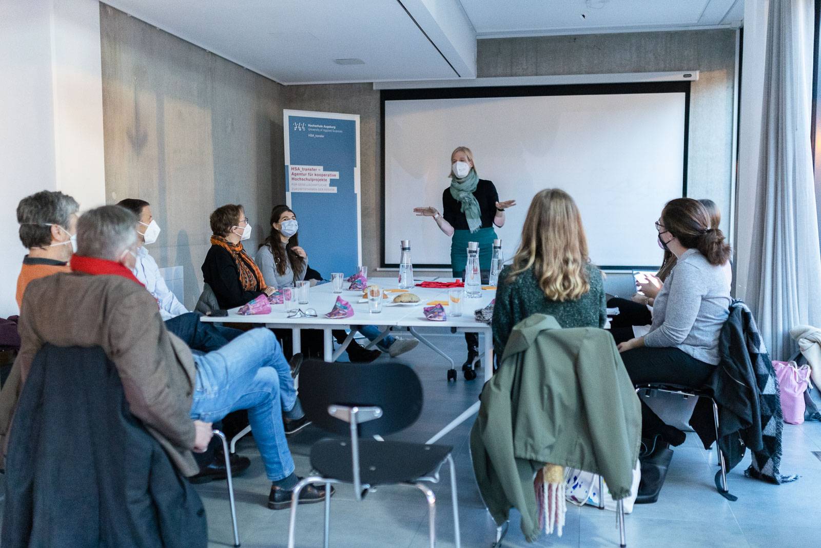 Prof. Dr. Barbara Rink vom Studiengang Soziale Arbeit der Hochschule Augsburg begrüßt gemeinsam mit den Studierenden die Transferpartner aus der Stadt Augsburg (links im Bild) im HSA_transmitter – dem Innovationsraum der Hochschule Augsburg.