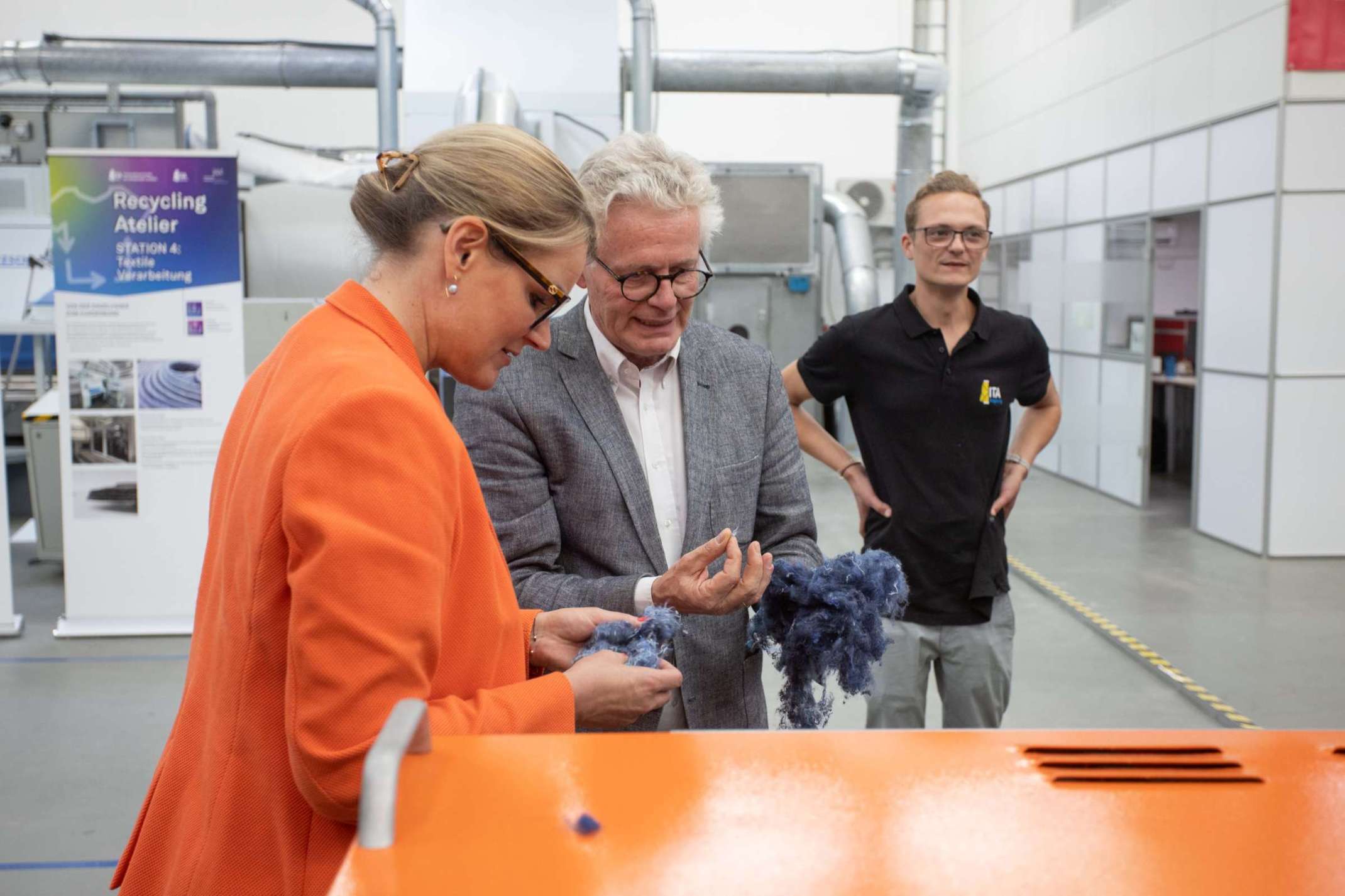 Augsburgs Oberbürgermeisterin Eva Weber lässt sich von Prof. Dr.-Ing. Stefan Schlichter den Prozessschritt des Schneidens von Textilien zeigen.