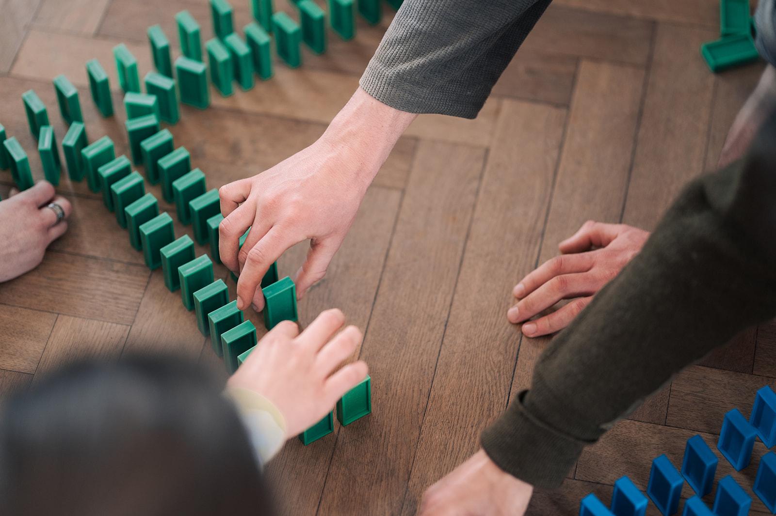 Hände, die gemeinsam mit Dominosteinen etwas bauen