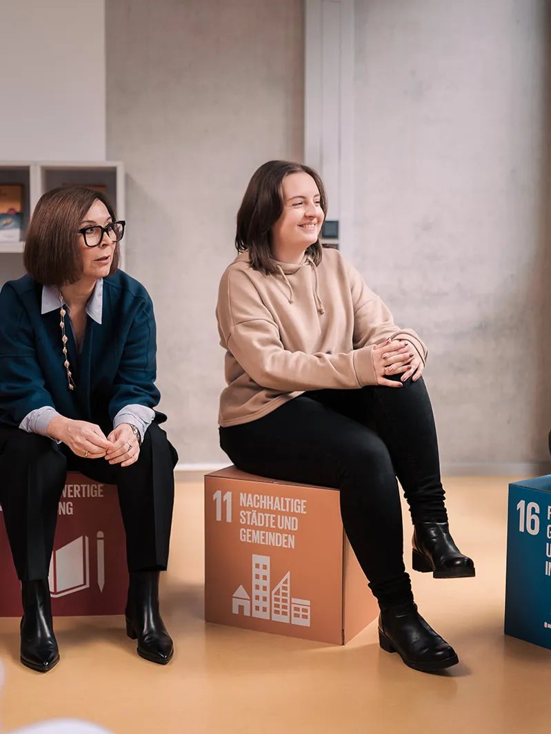 Professor Joeris sitzt neben einer Studentin auf Würfeln mit der Aufschrift jeweils eines Sustainability Development Goals der Vereinten Nationen.